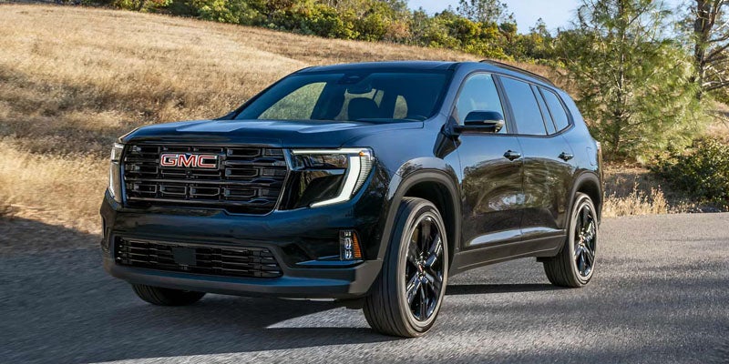 2026 GMC Acadia blue vehicle parked on a road outdoors surrounded by trees representing