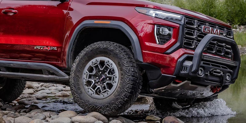 2026 GMC Canyon AT4X trim with off-road tires and suspension driving through rocky terrain