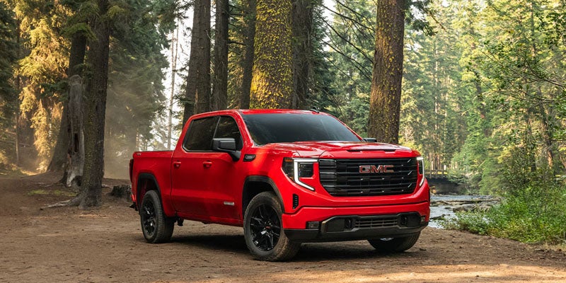 Red 2026 GMC Sierra 1500 driving on a forest trail showcasing strong off-road performance.