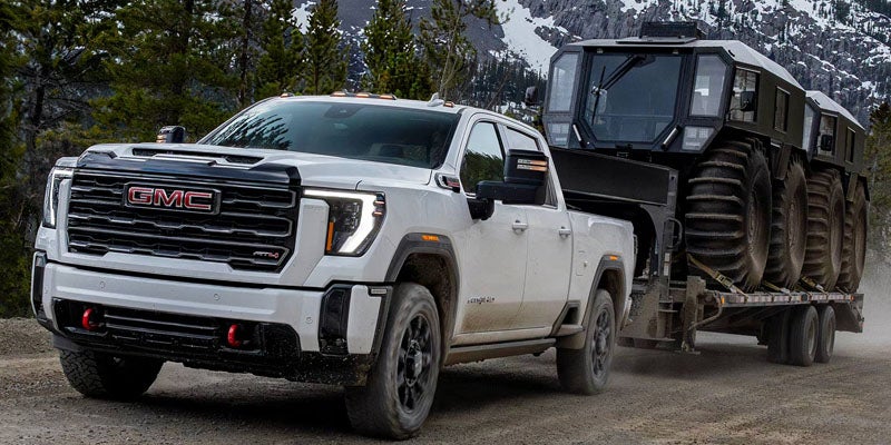 2026 GMC Sierra 2500 HD towing heavy equipment trailer through rugged mountain terrain.