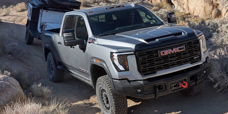 2026 GMC Sierra 2500 HD towing a trailer on a rugged mountain trail.